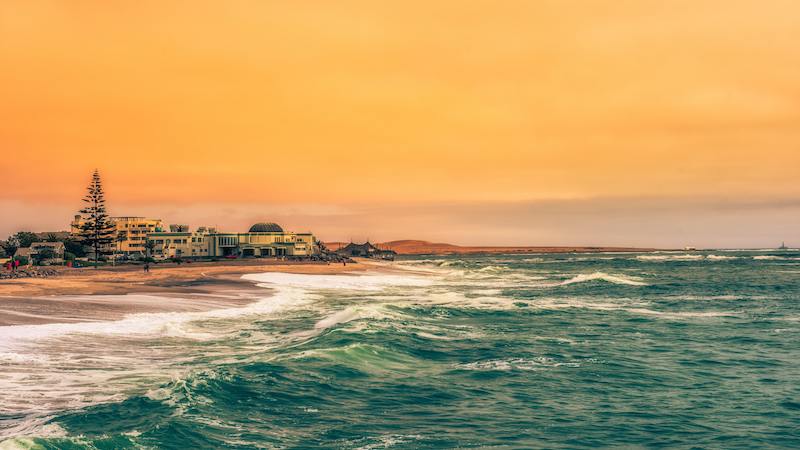 As the sun sets over the coastal town of Swakopmund in Namibia, the sea and the town are painted in a brilliant orange hue, a beautiful scenery for tourists on their luxury Namibia travels