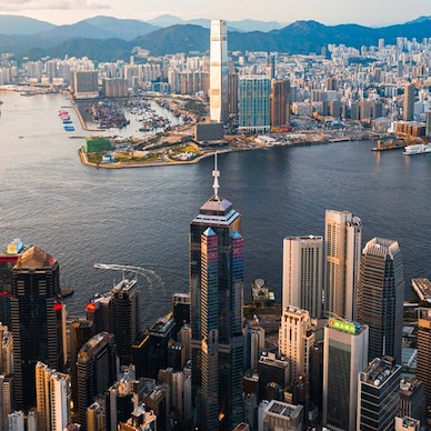 An aerial view of the entire Hong Kong city skyline, the blue mountains in the backdrop and the glistening waters of the Victoria Harbour